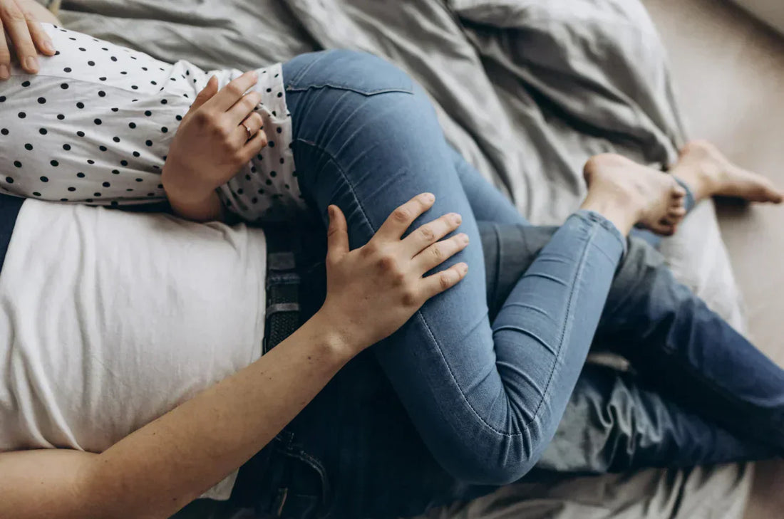 Couple allongé sur un lit, enlacé, mains sur la taille et les jambes en jean.