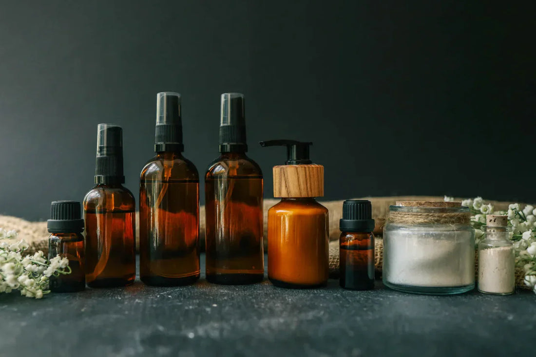 Alignement de flacons cosmétiques en verre ambré et pots de soin sur fond sombre.