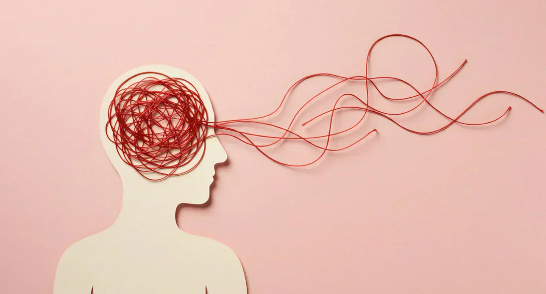 Silhouette de tête sur fond rose avec un enchevêtrement de fils rouges sortant du cerveau, symbole d’anxiété.