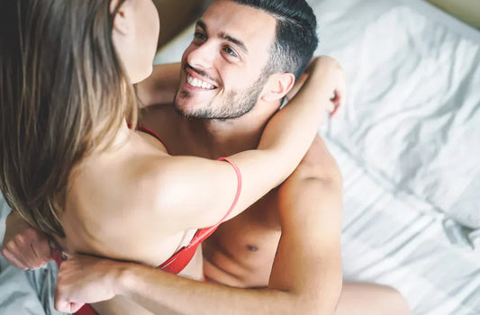 Couple enlacé sur un lit, regard complice et sourires.