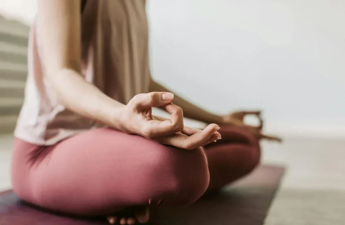 Personne assise en tailleur sur un tapis, main en mudra, en posture de méditation.