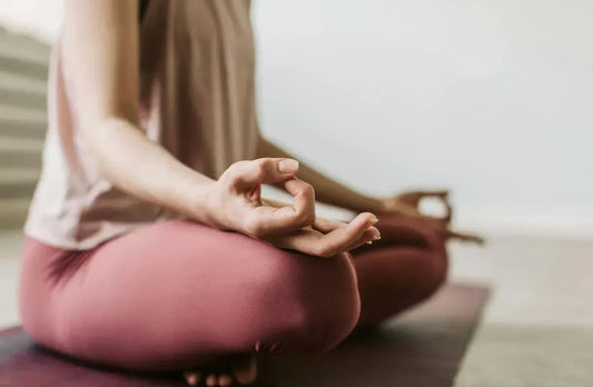 Personne assise en tailleur sur un tapis, main en mudra, en posture de méditation.