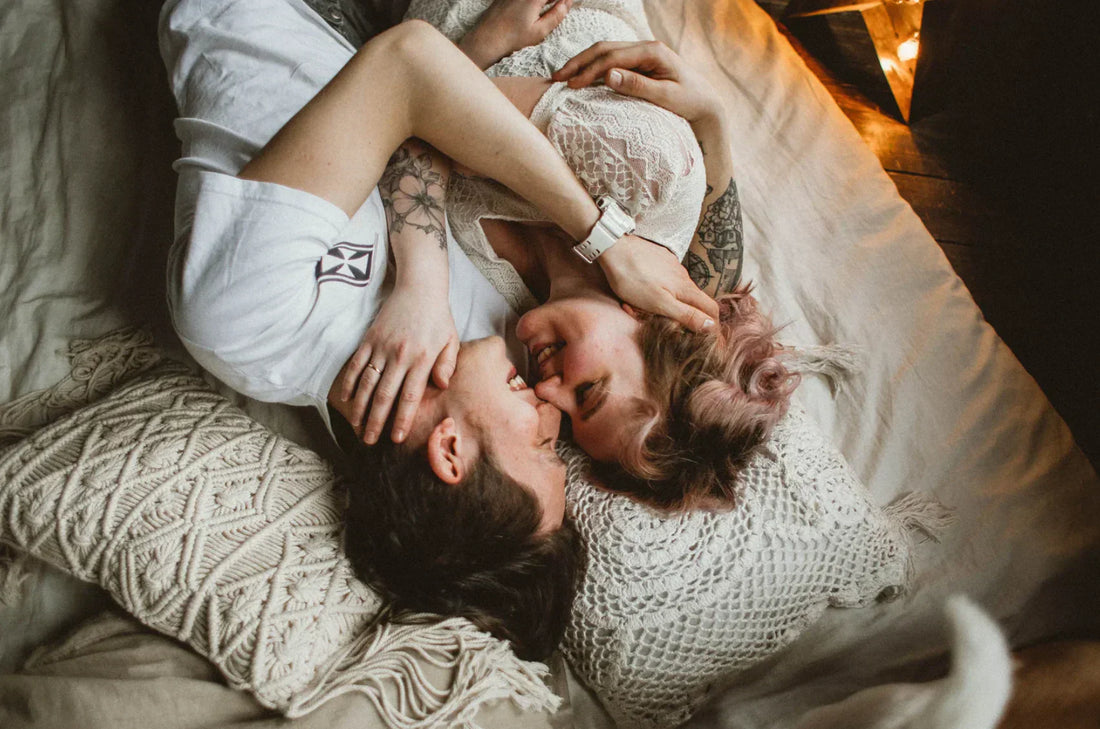 Couple allongé sur un lit, se souriant et se serrant dans les bras, ambiance chaleureuse.