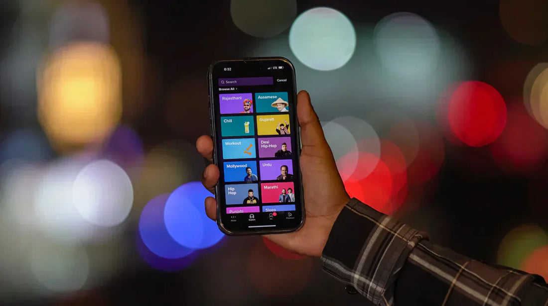 Main tenant un smartphone affichant une appli de musique, avec lumières floues de ville en arrière-plan.