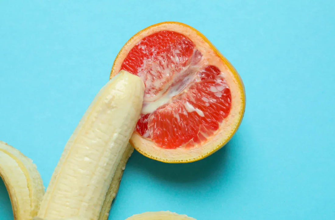 Banane partiellement épluchée posée près d’un demi-pamplemousse sur fond bleu.