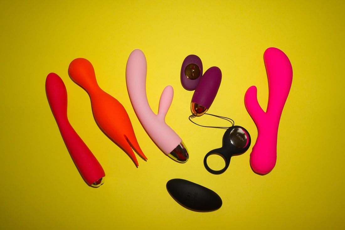 « Assortiment de sextoys colorés (vibromasseurs et accessoires) disposés sur fond jaune. »