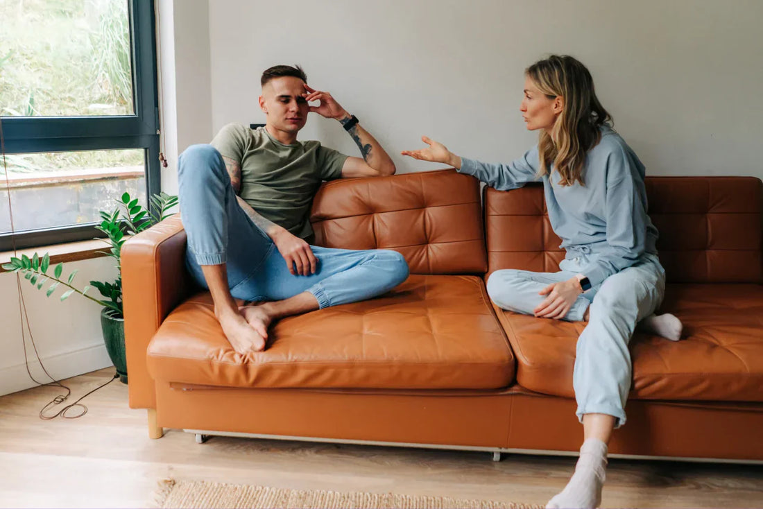 Couple assis sur un canapé en discussion, femme gesticulant, homme pensif.