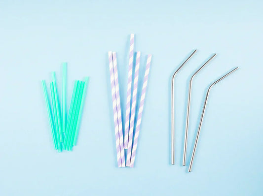 pailles en plastique vert, en papier rayé violet et en métal inox sur fond bleu.