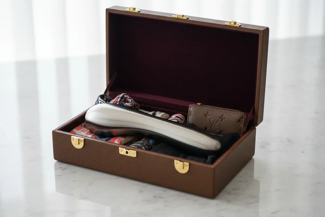 Valise ouverte sur une table contenant un objet métallique type masseur, avec des accessoires rangés à l’intérieur.