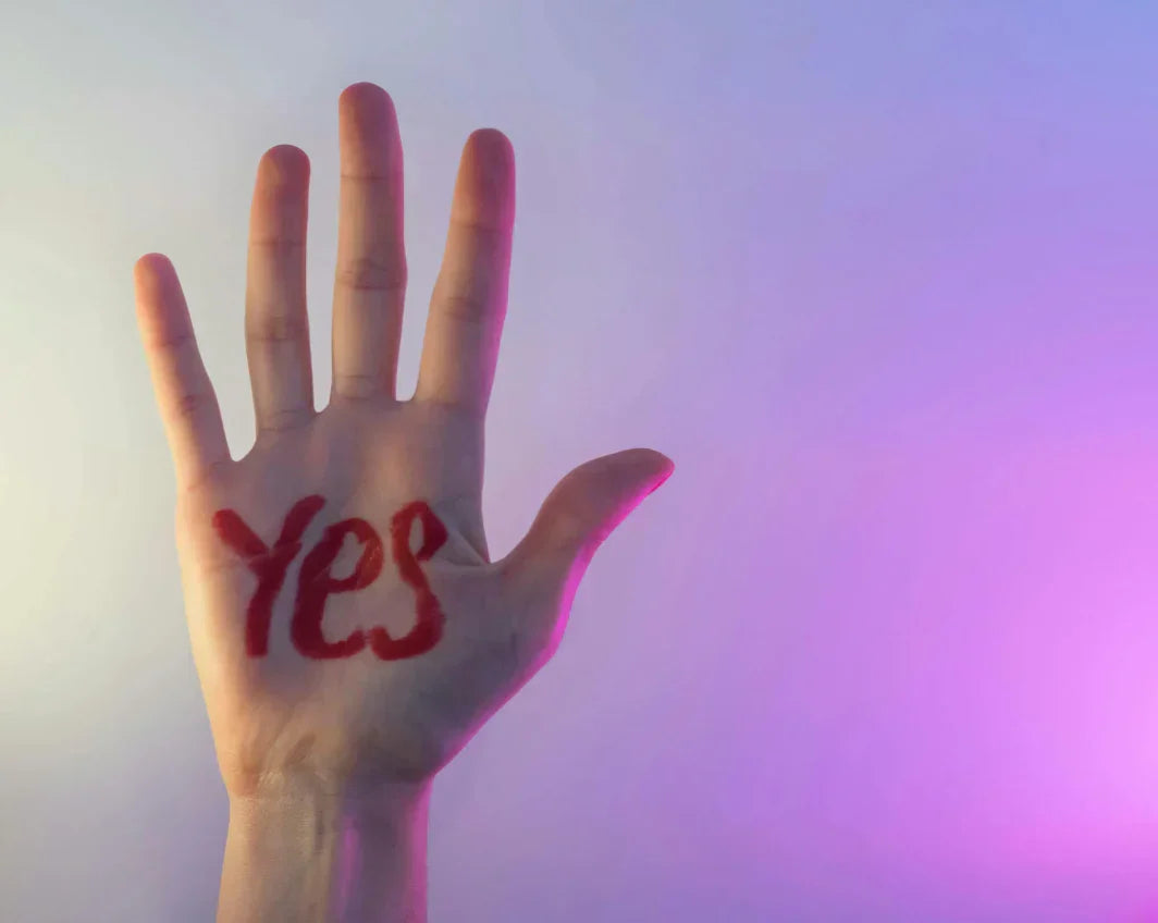 Main levée avec le mot “YES” écrit en rouge sur la paume, fond dégradé violet.